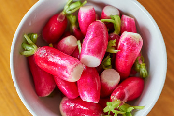 Freshly washed radish in a white bowl with wooden table in the background