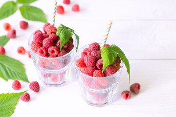 healthy eating concept: fresh raspberries in glasses and cocktail straws. background with fresh raspberries and green leaves.