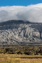 An icelandic mountain slope, under a blue sky and a blanket of clouds, showing a peculiar erosion pattern