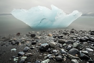 In a solitary beach in Iceland, a small iceberg lies stranded surrounded by pebbles