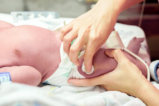 Image of nurse hands using cotton wool swab with alcohol to clean the baby's leg skin before vaccination.