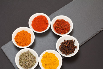 Various ground spices and herbs on stone cutting board.