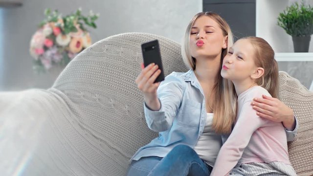 Happy young mother and teen daughter posing taking selfie using smartphone relaxing at home