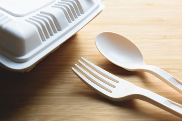 Biodegradable plastic lunch box, spoon and fork made from starch on wooden background