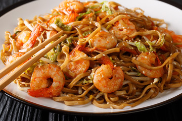 Tasty chow mein noodles with shrimp, vegetables and sesame seeds close-up on a plate on the table. horizontal