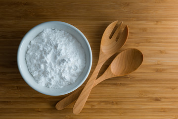 Top view tapioca starch/flour powder in white bowl with wooden background, spoon and fork
