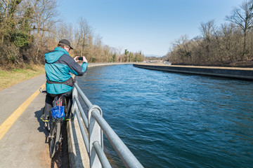 Man on a bicycle is taking a picture. Travel and active lifestyle concept. Pedestrian cycle track along the initial stretch of the Villoresi canal between Somma Lombardo and Castelnovate, Italy  