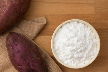 Top view of sweet potato starch in white bowl with sweet potato wooden table background