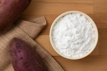 Top view of sweet potato starch in white bowl with sweet potato wooden table background