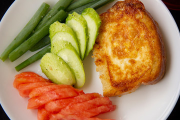toast fried in a beaten egg lies on a white plate with chopped tomatoes, cucumbers and green onions. Great breakfast. serving dishes on a black tablecloth