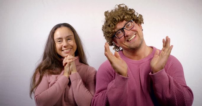 comically joyful man and woman are holding folded palms and looking to camera, smiling factitious