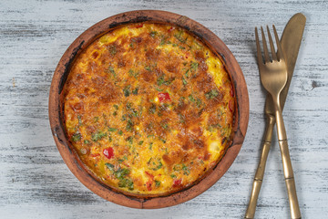 Ceramic bowl with vegetable frittata, simple vegetarian food. Frittata with tomato, pepper, onion and cheese on wooden table, close up. Italian egg omelette