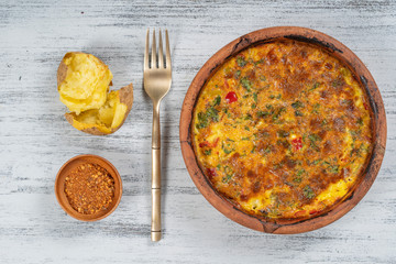 Ceramic bowl with vegetable frittata, simple vegetarian food. Frittata with tomato, pepper, onion and cheese on wooden table, close up. Italian egg omelette