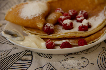 pancakes on a plate with raspberries and sprinkled with powdered sugar. Holiday - Shrovetide. round treat