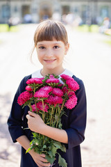 Fototapeta premium schoolgirl with bouquet in school uniform on background of school