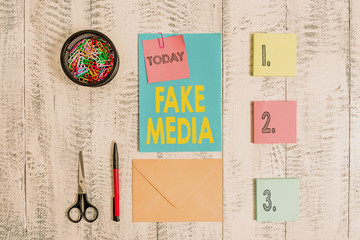 Word writing text Fake Media. Business photo showcasing An formation held by brodcasters which we cannot rely on Envelope letter sticky note ballpoint clips can scissors wooden background