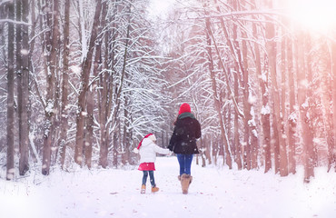 A winter fairy tale, a young mother and daughter  in the forest. A girl on a sled with gifts on the eve of the new year in the park. Two sisters walk in a New Year's park and ride a sled with gifts.
