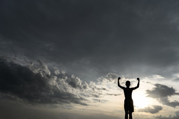 The boy raised his hand in the sky to ask for rain during the sunset.