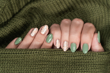 Closeup top view of two beautiful hands of white woman with fresh modern stylish manicure of green and beige pastel colors. Hands isolated on green knitted texture background. 