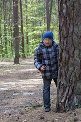 boy playing in the forest,boy with a stick in the forest behind a tree stands, pine forest