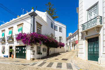 A picturesque street in Tavira with whitewashed houses decorated with bougainvillea flower,  Algarve, Portugal
