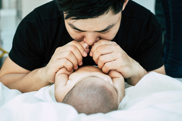 A young Asian father is sniffing his newborn baby.