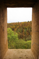 view to the beautiful colorful autumn forest through the window in stone wall of the old castle