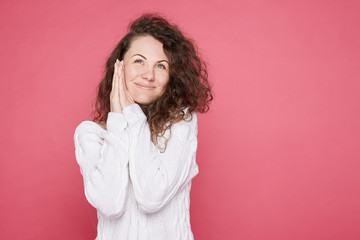 Blue eyed pretty woman in good mood dreams about something pleasant, imagines unforgettable episodes or moments in life, smiles gently, looking up, stands against pink studio wall with copy space.