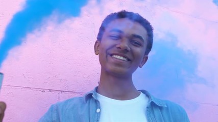 Afro-american boy waving blue smoke bomb, celebrating life, entertainment