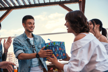 Giving present. Young happy man is receiving a gift from one of his friend while standing on the roof