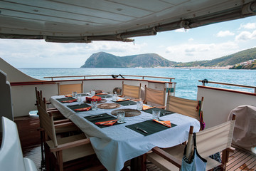 Naklejka premium Table set for breakfast on the rear deck of a luxury private yacht, cruising the mediterranean sea and docked in front of Lipari Island.