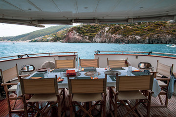 Table set for breakfast on the rear deck of a luxury private yacht, cruising the mediterranean sea and docked in front of Lipari Island.