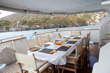 Table set for breakfast on the rear deck of a luxury private yacht, cruising the mediterranean sea and docked in front of Lipari Island.
