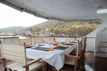 Table set for breakfast on the rear deck of a luxury private yacht, cruising the mediterranean sea and docked in front of Lipari Island.