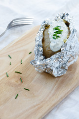 Ofenkartoffel in Aluminiumfolie mit Kräuterquark auf einem Holzbrett serviert