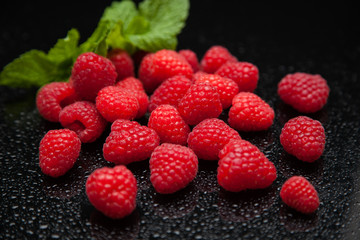 raspberries with mint leaves reflected on a black mirror table