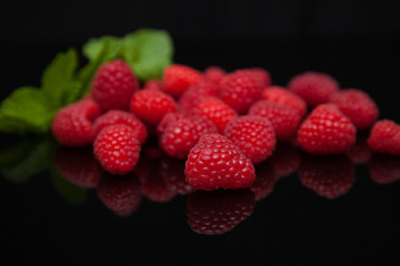 raspberries with mint leaves reflected on a black mirror table