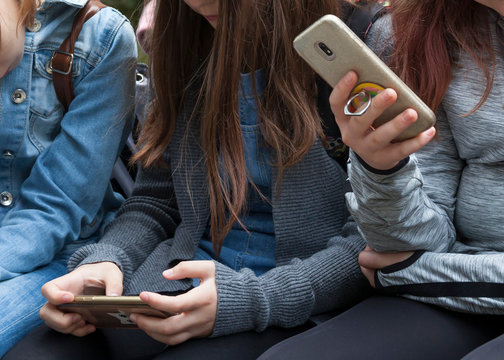 Two young teenage girls sitting holding smartphones in their hands. Teens, kids playing around, checking their phones Phone addiction or young preteens using modern technology in everyday life concept