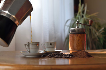 Coffee is pouring from a moka pot to two cups