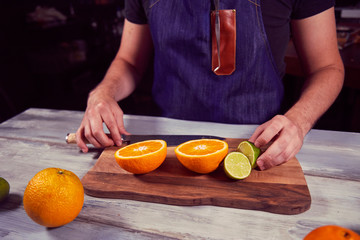 Young chef in kitchen cut orange and lime. Food concept.