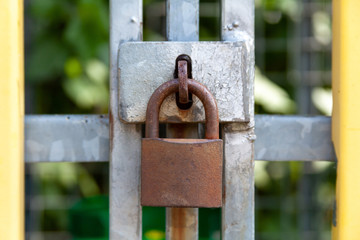 A closed rusty steel padlock frame on a metal reinforcement closeup, frontal shot. Safety and security simple abstract symbol concept, Old iron pad lock placed on the gate in the centre, garden behind