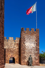 Entrance of Silves castle with statue of King Sancho I of Portugal and a big Portuguese flag on the tower.