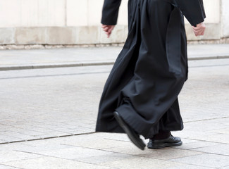 Catholic priest in the black cassock walking on the street solo, only legs visible. Clergy, faith,...