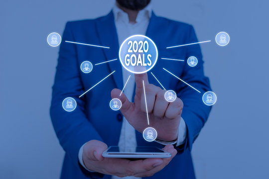 Text sign showing 2020 Goals. Business photo showcasing A plan to do for something new and better for the coming year Male human wear formal work suit presenting presentation using smart device