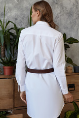 Medium full back shot of a young European lady dressed in a white long-sleeved tunic shirt and a...