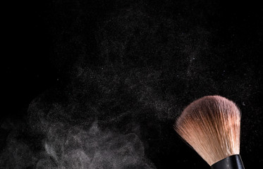cosmetic brush and sprayed cloud of cosmetics on a black background