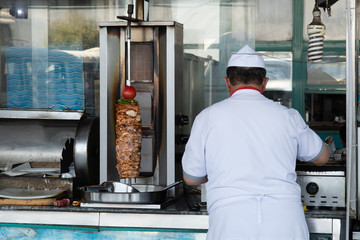 Unidentifiable Turkish Doner Kebab vendor. Fast food eatery, chicken kebab on skewer. Chef at...