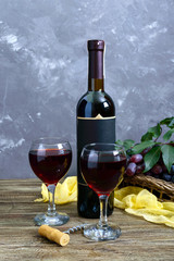 Wineglasses with red wine, bottle, corkscrew, blue grapes, leaves on a wooden table.  Vertical view