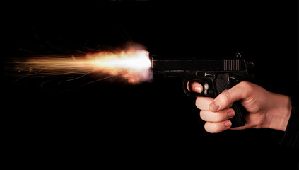 Gun in hand on black background. The threat of a firearm during a robbery on a dark street. Assault...