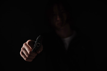 Gun in hand on black background. The threat of a firearm during a robbery on a dark street. Assault with a semiautomatic weapon.